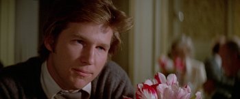 Movie still from “Winter Kills” (1979), directed by William Richert – A man sitting in front of some flowers; Close Up shot, Over the shoulder angle