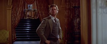 Movie still from “Winter Kills” (1979), directed by William Richert – A man in a suit and tie standing in front of a staircase; Medium shot, Low angle