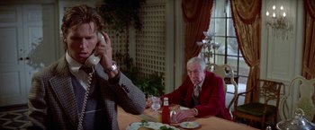 Movie still from “Winter Kills” (1979), directed by William Richert – An older man sitting at a dinner table talking on the phone; Medium shot, Low angle