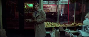 Movie still from “Winter Kills” (1979), directed by William Richert – A man standing in front of a store holding a tray; Medium shot, Over the shoulder angle