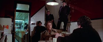 Movie still from “Winter Kills” (1979), directed by William Richert – A group of men sitting at a table in a room; Wide shot, High angle
