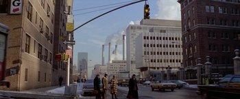 Movie still from “Winter Kills” (1979), directed by William Richert – A group of people walking across a street near buildings; Extreme Wide shot, Low angle