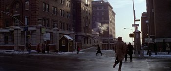 Movie still from “Winter Kills” (1979), directed by William Richert – A group of people walking down a street near a building; Extreme Wide shot, High angle