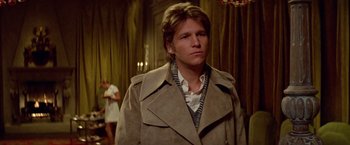 Movie still from “Winter Kills” (1979), directed by William Richert – A man in a trench coat standing in a room; Close Up shot, Over the shoulder angle