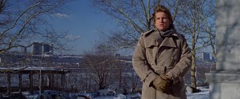Movie still from “Winter Kills” (1979), directed by William Richert – A man in a trench coat standing in front of a tree; Medium shot, Low angle