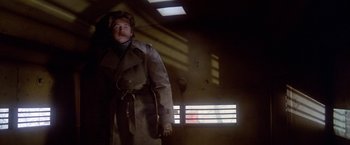 Movie still from “Winter Kills” (1979), directed by William Richert – A man in a trench coat standing next to a window; Medium shot, Low angle