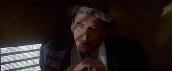 Movie still from “Winter Kills” (1979), directed by William Richert – A man in a suit and a hat is looking at the camera; Close Up shot, High angle