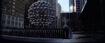 Movie still from “Winter Kills” (1979), directed by William Richert – A fountain in the middle of a city with buildings in the background; Extreme Wide shot, High angle