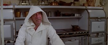 Movie still from “Winter Kills” (1979), directed by William Richert – An older man wearing a white robe in a kitchen; Close Up shot, Over the shoulder angle