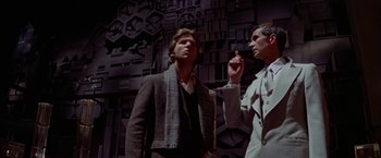 Movie still from “Winter Kills” (1979), directed by William Richert – Two men standing next to each other in front of a wall; Medium shot, Low angle