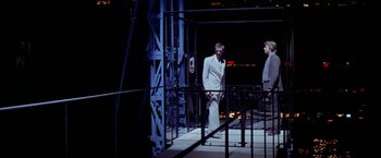 Movie still from “Winter Kills” (1979), directed by William Richert – A man standing next to two other men; Wide shot, Over the shoulder angle