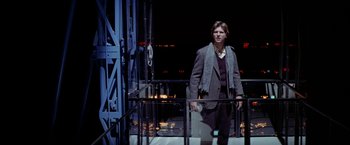 Movie still from “Winter Kills” (1979), directed by William Richert – A man standing on top of a metal railing next to a building; Medium shot, Low angle