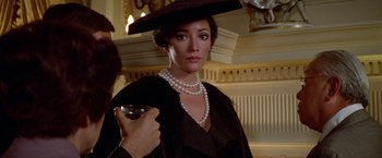 Movie still from “Winter Kills” (1979), directed by William Richert – A woman wearing a hat and holding a glass of wine; Close Up shot, Over the shoulder angle