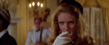 Movie still from “Winter Kills” (1979), directed by William Richert – A woman drinking a glass of wine in front of a man in a suit; Close Up shot, Low angle