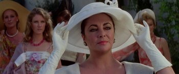 Movie still from “Winter Kills” (1979), directed by William Richert – A woman wearing a white hat and gloves; Close Up shot, Over the shoulder angle