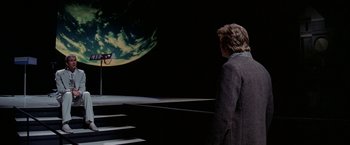 Movie still from “Winter Kills” (1979), directed by William Richert – A man standing in front of a wall with a picture on it; Extreme Wide shot, Over the shoulder angle