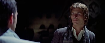 Movie still from “Winter Kills” (1979), directed by William Richert – A man wearing a jacket and a scarf sitting down; Close Up shot, Over the shoulder angle