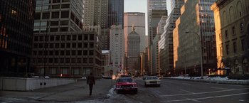 Movie still from “Winter Kills” (1979), directed by William Richert – A street scene with a person walking on the sidewalk and cars on the street; Extreme Wide shot, High angle