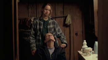 Movie still from “Winter's Bone” (2010), directed by Debra Granik – A woman standing next to a man in front of a wooden wall; Medium shot, Over the shoulder angle