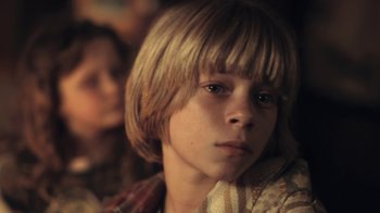 Movie still from “Winter's Bone” (2010), directed by Debra Granik – A young boy with blonde hair sitting in front of a group of people; Close Up shot, Low angle
