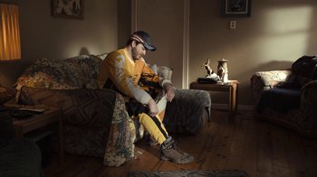 Movie still from “Winter's Bone” (2010), directed by Debra Granik – A man sitting on a couch in a living room; Wide shot, High angle