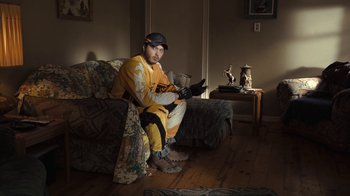 Movie still from “Winter's Bone” (2010), directed by Debra Granik – A man sitting on top of a couch in a living room; Medium shot, Low angle