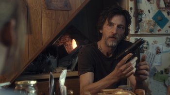 Movie still from “Winter's Bone” (2010), directed by Debra Granik – A man sitting in front of a fireplace holding a cell phone; Close Up shot, Over the shoulder angle