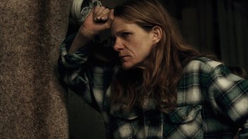 Movie still from “Winter's Bone” (2010), directed by Debra Granik – A woman in a plaid shirt leaning against a wall; Close Up shot, High angle