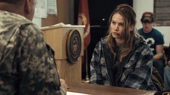 Movie still from “Winter's Bone” (2010), directed by Debra Granik – A woman sitting at a table in front of a podium; Medium shot, Over the shoulder angle