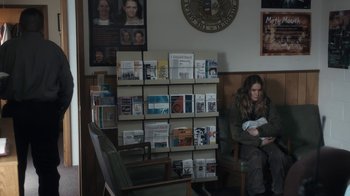 Movie still from “Winter's Bone” (2010), directed by Debra Granik – A woman sitting on a chair in front of a wall of books; Medium shot, Over the shoulder angle