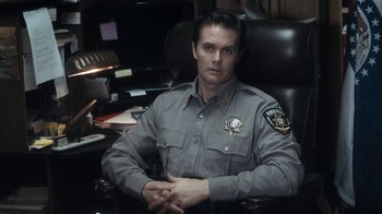 Movie still from “Winter's Bone” (2010), directed by Debra Granik – A police officer sitting at a desk in his office; Medium shot, Over the shoulder angle