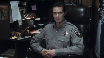 Movie still from “Winter's Bone” (2010), directed by Debra Granik – A police officer sitting at a desk in his office; Medium shot, Over the shoulder angle