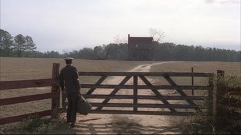 Movie still from “Wise Blood” (1979), directed by John Huston – A man standing in front of an open gate; Wide shot, High angle