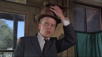 Movie still from “Wise Blood” (1979), directed by John Huston – A man in a suit and tie holding his hat up; Close Up shot, Low angle