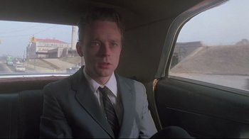 Movie still from “Wise Blood” (1979), directed by John Huston – A man in a suit and tie sitting in the back of a car; Close Up shot, Low angle