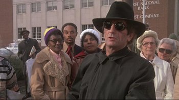 Movie still from “Wise Blood” (1979), directed by John Huston – A group of people standing next to each other on the street; Medium shot, Low angle