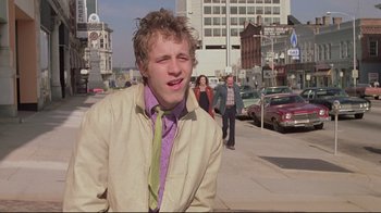 Movie still from “Wise Blood” (1979), directed by John Huston – A man in a beige jacket and a green tie; Medium shot, Low angle