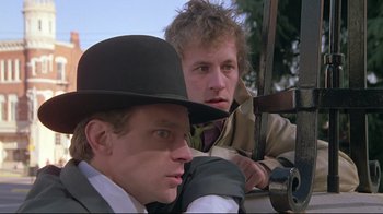 Movie still from “Wise Blood” (1979), directed by John Huston – Two men in hats and coats are sitting next to each other; Close Up shot, Low angle