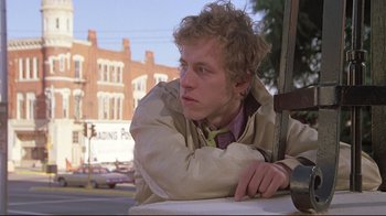 Movie still from “Wise Blood” (1979), directed by John Huston – A young man leaning on the side of the road; Close Up shot, Low angle