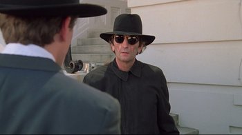Movie still from “Wise Blood” (1979), directed by John Huston – A man in a hat and sunglasses looking at another man in a suit; Medium shot, Over the shoulder angle