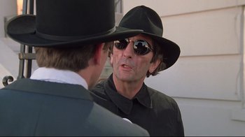 Movie still from “Wise Blood” (1979), directed by John Huston – A man wearing a hat and sunglasses talking to another man; Close Up shot, Over the shoulder angle