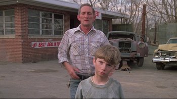 Movie still from “Wise Blood” (1979), directed by John Huston – A man and a boy standing in front of a building; Medium shot, Low angle