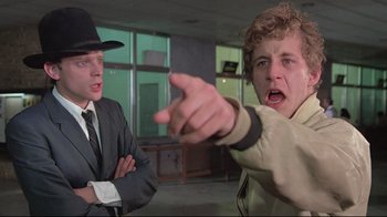 Movie still from “Wise Blood” (1979), directed by John Huston – A man pointing at another man wearing a suit and hat; Medium shot, Low angle