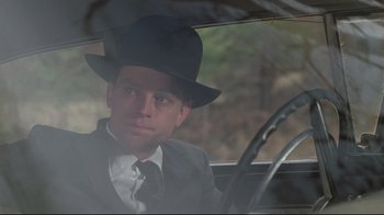 Movie still from “Wise Blood” (1979), directed by John Huston – A man in a suit and hat sitting in the driver's seat of a car; Close Up shot, Over the shoulder angle