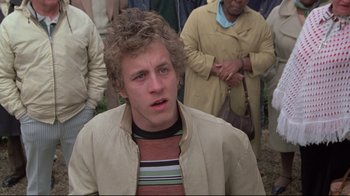 Movie still from “Wise Blood” (1979), directed by John Huston – A young man in a beige jacket is looking at the camera; Close Up shot, Over the shoulder angle