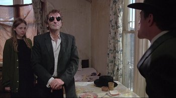 Movie still from “Wise Blood” (1979), directed by John Huston – A man in a suit sitting at a dining table; Medium shot, Low angle