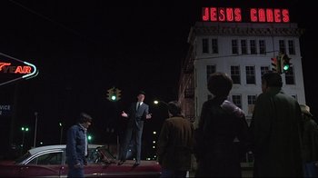 Movie still from “Wise Blood” (1979), directed by John Huston – A man standing on a platform in front of a building; Wide shot, Low angle