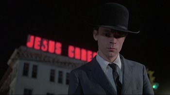 Movie still from “Wise Blood” (1979), directed by John Huston – A man wearing a suit and a top hat in front of a building; Close Up shot, Low angle