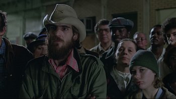 Movie still from “Wise Blood” (1979), directed by John Huston – A group of people standing in a room; Medium shot, Over the shoulder angle