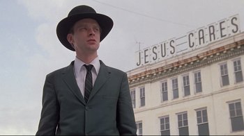 Movie still from “Wise Blood” (1979), directed by John Huston – A man in a suit and hat standing in front of a building; Close Up shot, Low angle